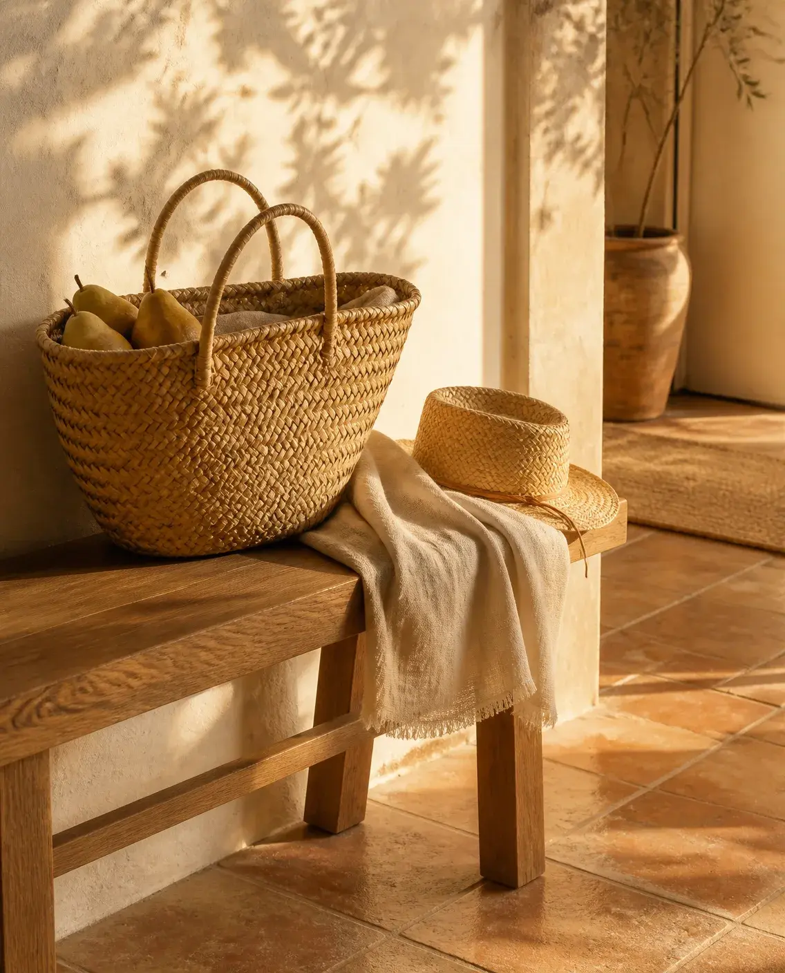 A woven market basket with pears, a linen scarf and a straw hat on an oak bench in warm late-afternoon light.